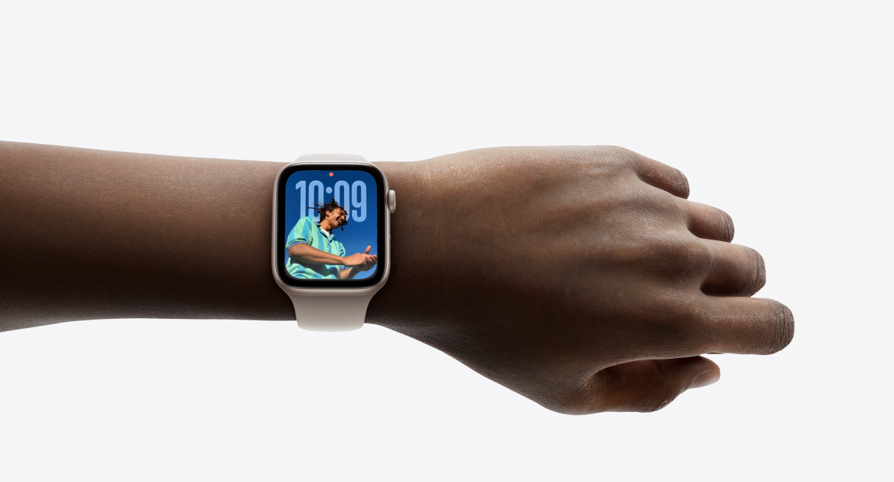 人物の手首に装着された、ラバーバンドと組み合わせたローズゴールドのApple Watchのクローズアップ。新しいLiquid Glassのデザインを示している