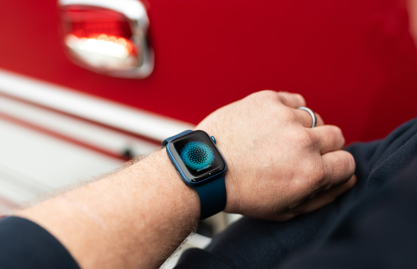 An arm wearing an Apple Watch displays the message: Now inhale, with a fire engine nearby