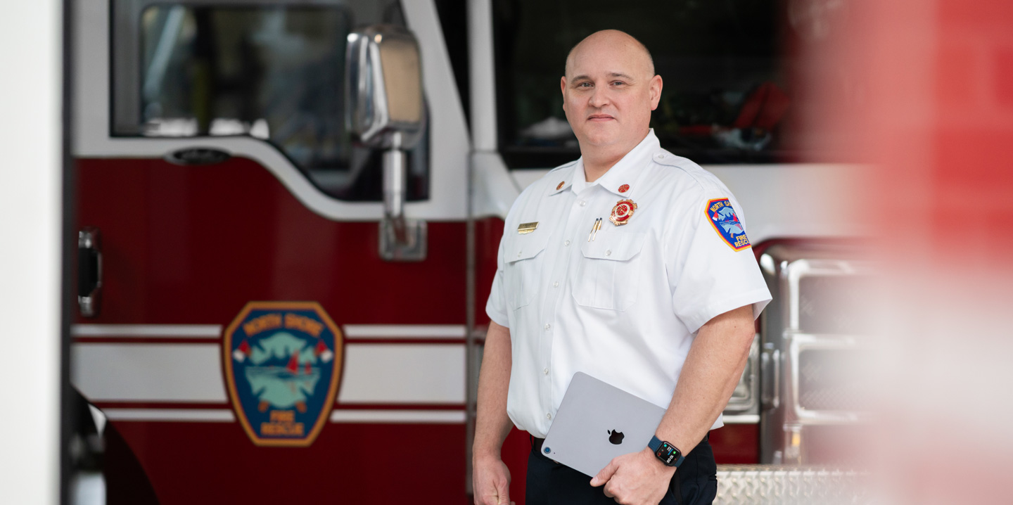 The fire chief stands in front of a fire engine holding an iPad and wearing an Apple Watch