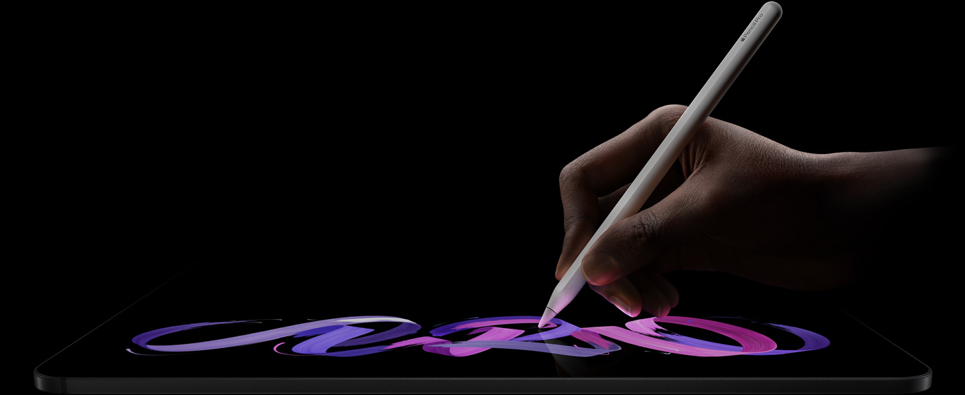 جهاز iPad Pro، الجزء الأمامي الخارجي، الوضع الأفقي، صورة جانبية، لون أسود فلكي، يد تحمل قلم Apple Pro أبيض اللون، ترسم تصميماً تجريدياً باللونين البنفسجي والوردي على الشاشة