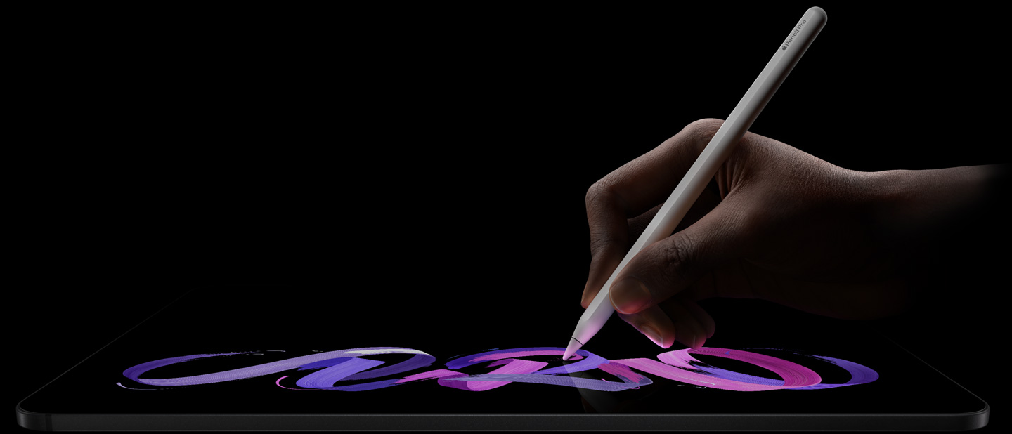 جهاز iPad Pro، الجزء الأمامي الخارجي، الوضع الأفقي، صورة جانبية، لون أسود فلكي، يد تحمل قلم Apple Pro أبيض اللون ترسم تصميماً تجريدياً باللونين البنفسجي والوردي على الشاشة