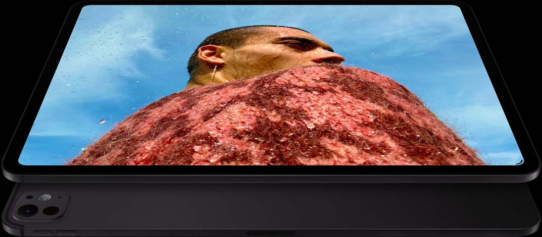 جهاز iPad Pro، الجزء الخارجي الجانبي الأمامي، الوضع الأفقي، لون أسود فلكي، زوايا مدورة، إطار شاشة أسود، شاشة تعرض صورة لرجل يرتدي سترة حمراء تحت سماء زرقاء، وتحته جهاز iPad Pro آخر، الجزء الخارجي الخلفي، الوضع الأفقي، لون أسود فلكي، نظام كاميرات Pro، زر رفع مستوى الصوت، زر خفض مستوى الصوت