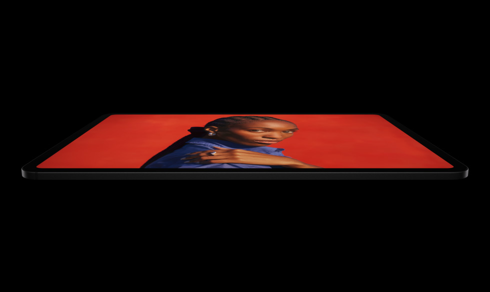 جهاز iPad Pro، الجزء الجانبي الخارجي، الوضع الأفقي، لون أسود فلكي، زوايا مدورة، إطار شاشة أسود، شاشة تعرض شاشة حمراء زاهية مع شخص يقف واضعاً يده على كتفه ويرتدي قميصاً أزرق