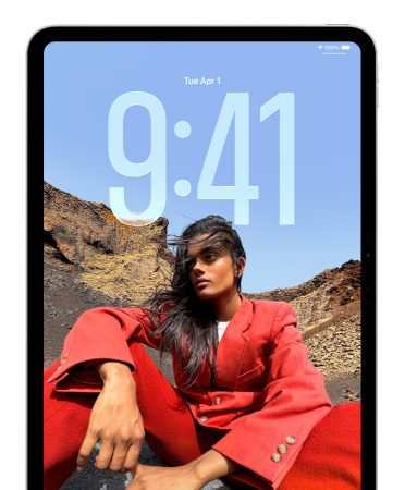 En iPad med låst skjerm viser klokkeslettet med store tall delvis gjemt bak bildet av en sittende person.